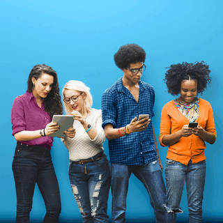 Dengan latar belakang biru, 4 anak muda melihat ponsel dan tablet mereka bersama-sama