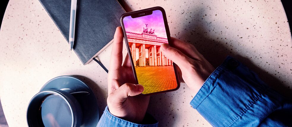 Someone is holding a smartphone above a bistro table. On the screen is a picture of the Brandenburg Gate.