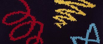 Close-up image of a knitted pullover with a red spiral and a yellow and blue zig-zag pattern 