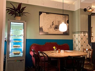 Cafe corner: vintage sofa, in front of it a wooden table, to the left of it a cake counter