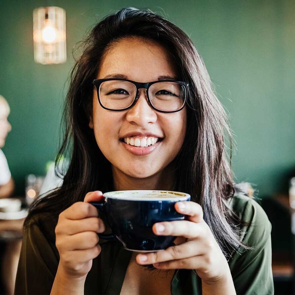 jovem garota segura xícara de café e sorri para a câmera