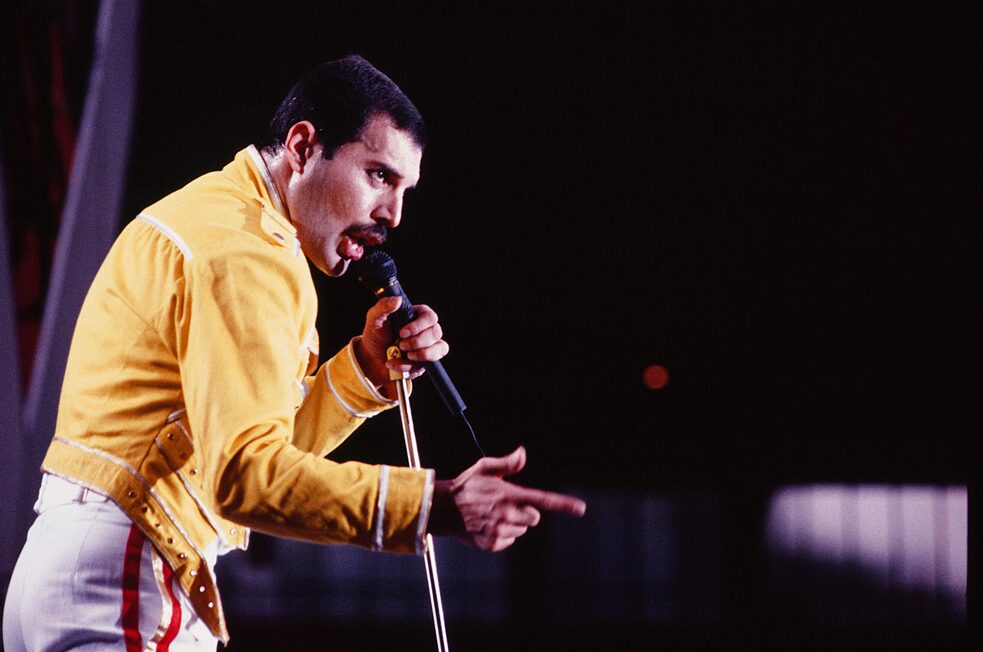 Ganz laut singen und das Vertrauen ins eigene Team stärken: „We are the champions!“ – Mega-Hit von Queen und Freddie Mercury, hier 1986 live on stage in Köln.