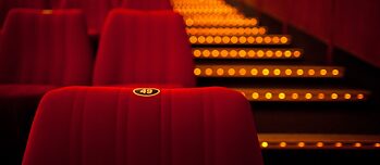 Foto de una sala de cine. En primer plano se ve una butaca roja con el número 49