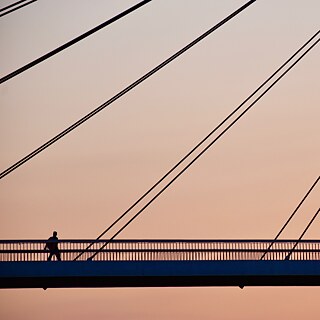 Ein Fußgänger geht auf einer Hängebrücke im Abendrot.