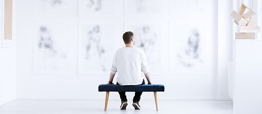 Ein Mann sityt auf der Bank und schaut Fotografien einer Gallerie an