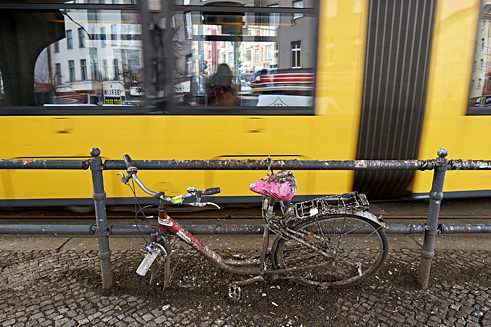 Kostra bicyklu stojí opřená o zábradlí, v pozadí projíždí tramvaj.