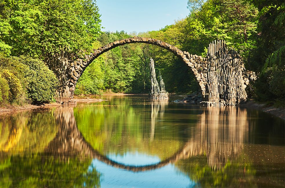 <b>Le pont Rakotz : le reflet parfait</b><br/>Si vous aimez les safaris photos, venez admirer le pont Rakotz dans le parc paysager de Kromlau en Saxe. Le site abrite le plus grand parc de rhododendrons d’Allemagne et un pont datant de 1882, également connu sous le nom de Pont du diable. Il se reflète dans l’eau du lac Rakotz dans une géométrie circulaire parfaite. Les colonnes de basalte qui s’élèvent hors de l’eau créent une atmosphère absolument magique.