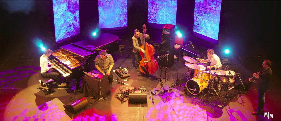 5 Musiker von oben gesehen auf Bühne mit Projektion