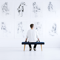 Mann sitzt in Museum vor Zeichnungen