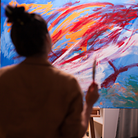 Une adolescente regarde un tableau et tient un pinceau dans sa main.