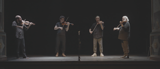 Vier Männer auf einer Bühne spielen Violine