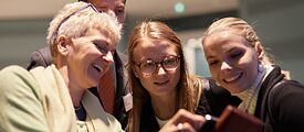 Three female participants of the EU-course 2017 Berlin look at a cell phone together and laugh