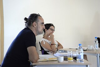 The picture shows two of the participants. The one in front is slightly blurred. The participant in the back has her hand raised thoughtfully to her face. Both are looking forward and listening intently.