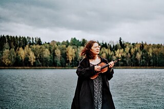 Noor naine looduses hoiab käes rahvalikku viiulit.
