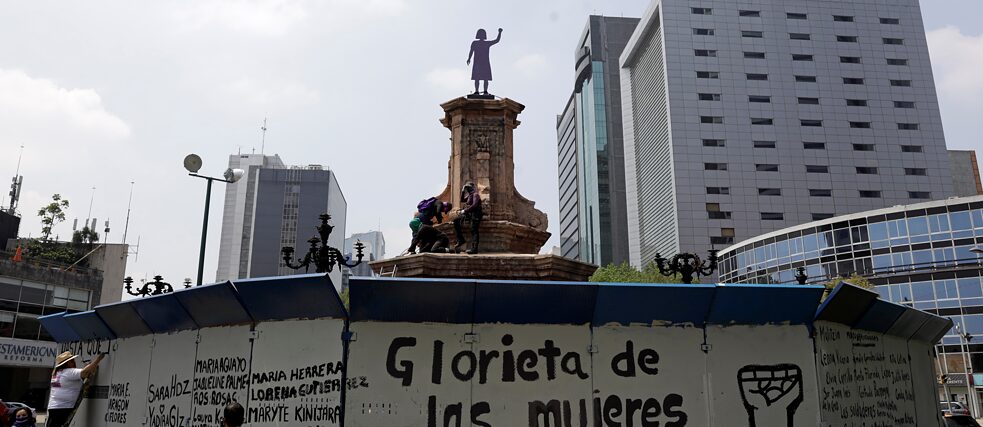 Frauen bemalen den Zaun, der den Ort schützt, auf dem einst die Statue von Christoph Kolumbus stand, nachdem Aktivist*innen am 25. September 2021 in Mexiko-Stadt ein Anti-Denkmal enthüllt hatten. 