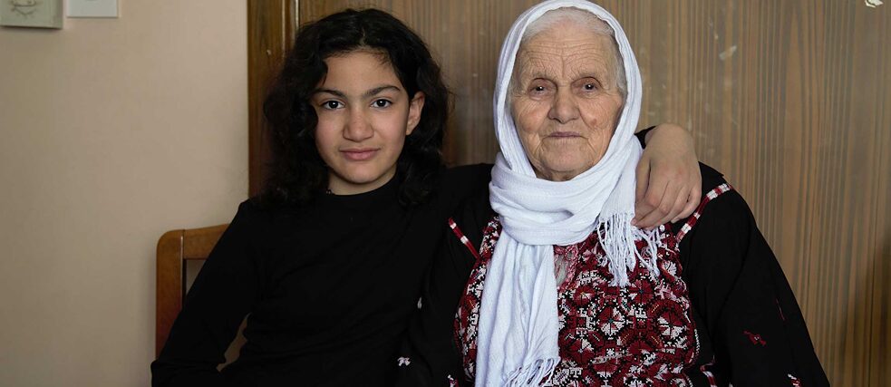 Foto von Thuraya, einem zwölfjährigen, modern gekleideten Mädchen, und Um-Reyad, einer älteren Frau in traditionellem bestickten Gewand