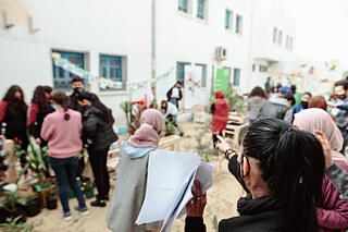 Eine Frau von hinten zeigt auf den Schulhof, wo vielen Personen Pflanzaktivitäten verrichten
