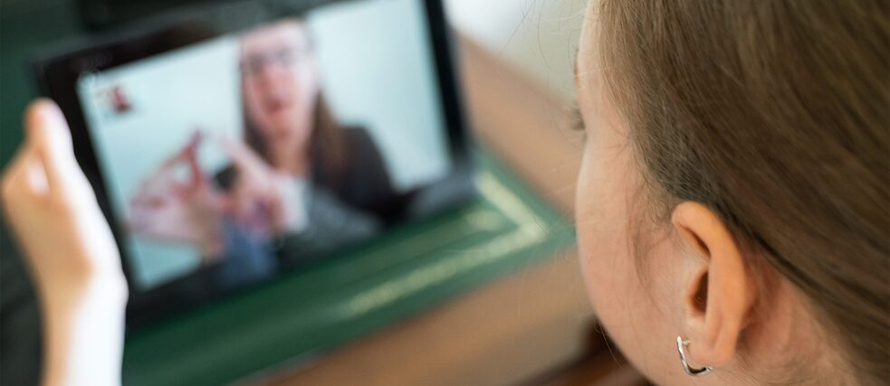A young female student looks at a screen with a teacher speaking.
