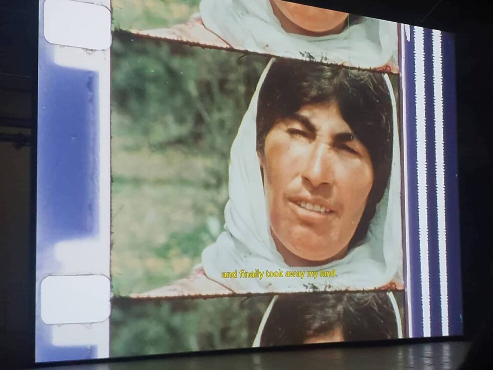 A projection that shows a photo frame with blue and white patterns that contains the photograph of a woman with dark hair who wears a head scarf.
