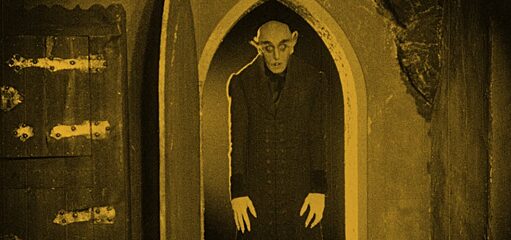 Nosferatu standing in a doorway in yellow light.