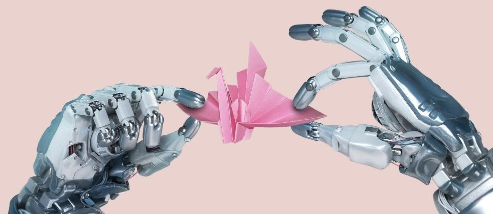 Zwei Roboter-Hände halten einen Origami Kranich. Der Hintergrund ist rosa und bietet Raum für redaktionellen Text.