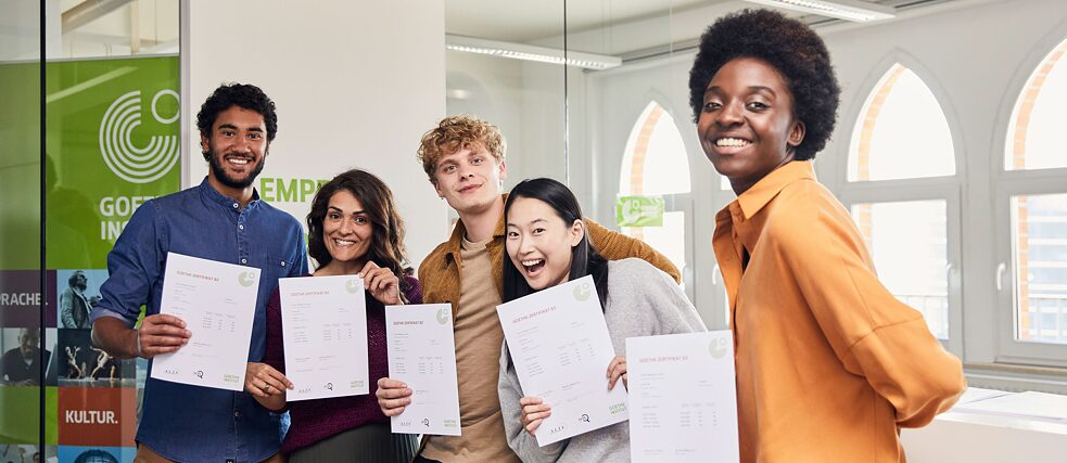 Молоді люди успішно склали мовний іспит Goethe-Institut. Вони щасливі і з гордістю показують свої сертифікати у камеру. Вони посміхаються.