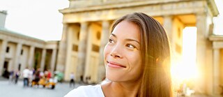 A young smiling woman stands in front of the Brandenburg Gate and looks upwards.