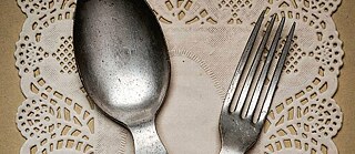 Close up of a knife and fork, crossed over one another, on a table covered with a white frilly serviette