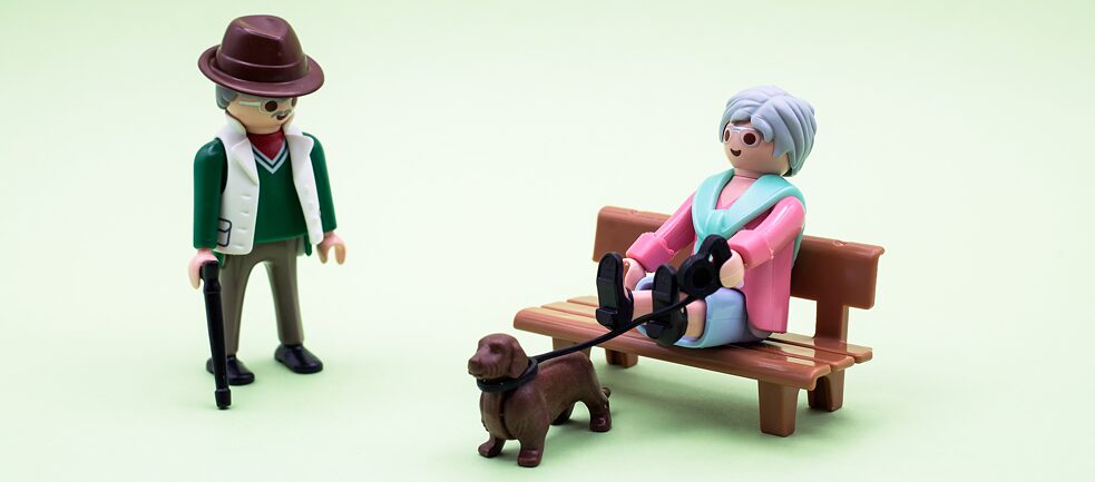 Un personnage se promène, un autre est assis sur un banc avec son chien en laisse