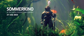 A diver figurine in an aquarium surrounded by goldfish and water plants. Air bubbles rise from the figurine.