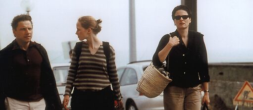 Scene from the film "The State I Am In": A man and a woman with their teenage daughter are walking along a street. The parents are carrying bags and the daughter a backpack. 