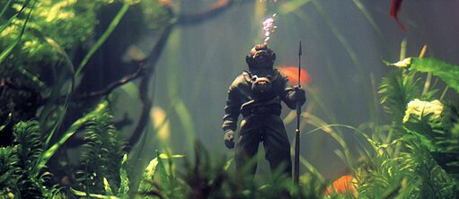 Scene from the film "Undine": : A diver figurine in an aquarium surrounded by goldfish and water plants. Air bubbles rise from the figurine.