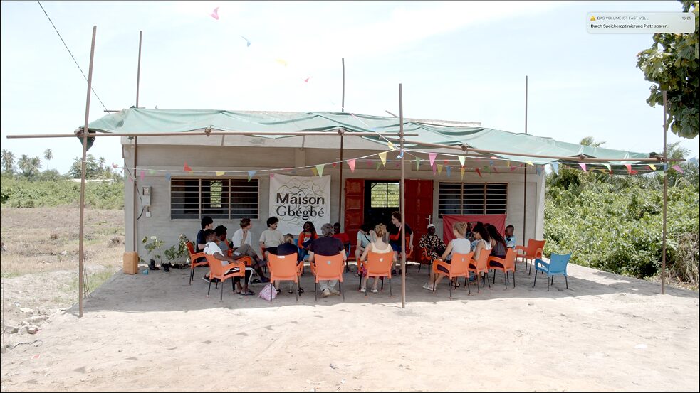 Vor dem temporären Versammlungsraum des Maison Gbegbe; Gregor Kasper und Musquiqui Chiying unterhalten sich mit Studenten der UdK und der Universität von Lome bei den Gbegbe-Tagen, Videostill, 2022