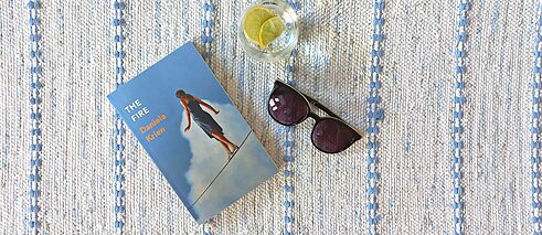 The book cover showing a woman balancing on a rope surrounded by sky, lying on a blanket with a pair of sunglasses and a drink