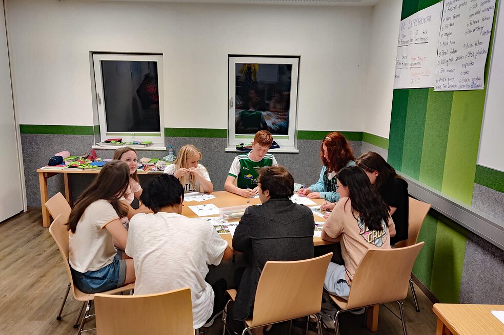 Jugendliche arbeiten konzentriert an einem großen Tisch in einem Klassenzimmer.