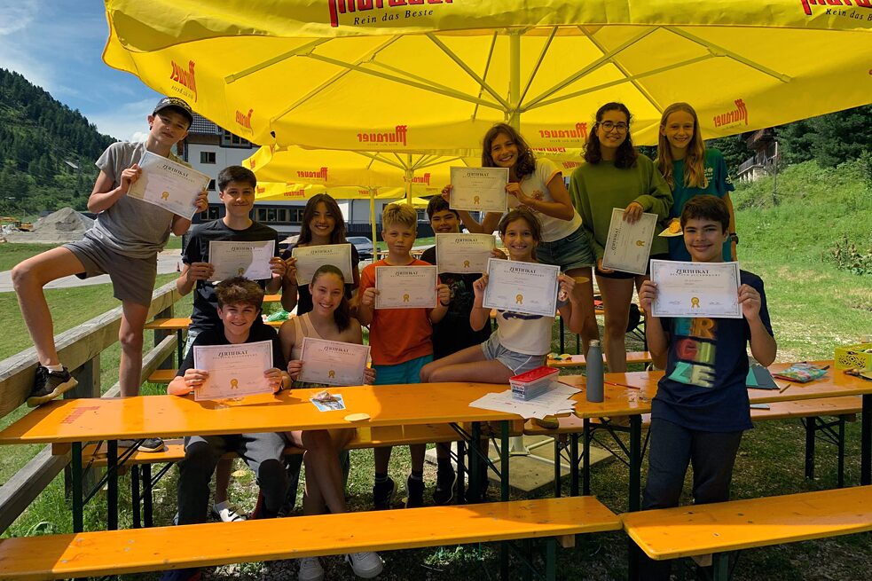 Jugendliche unter einem großen, gelben Sonnenschirm zeigen ihre Zertifikate.