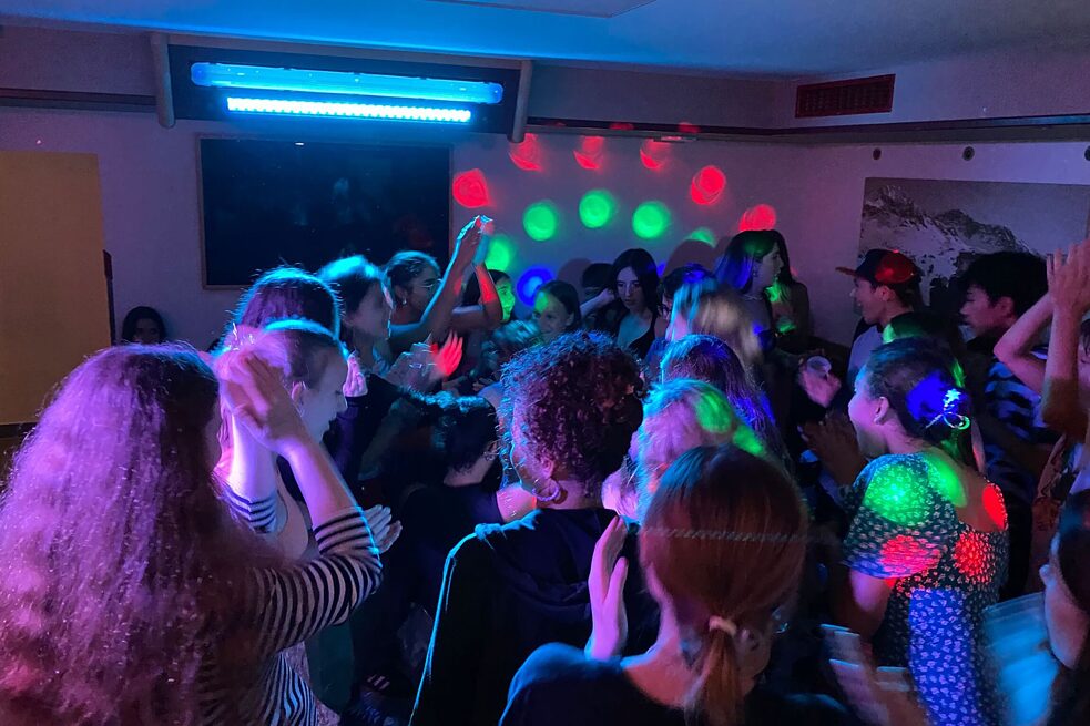 Jugendliche tanzen, der Raum ist mit guntem Neonlichtern geschmückt.