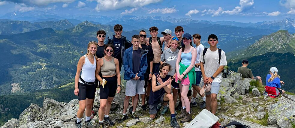 Eine kleine Gruppe Jugendlicher und junger Erwachsener auf einer Bergspitze.