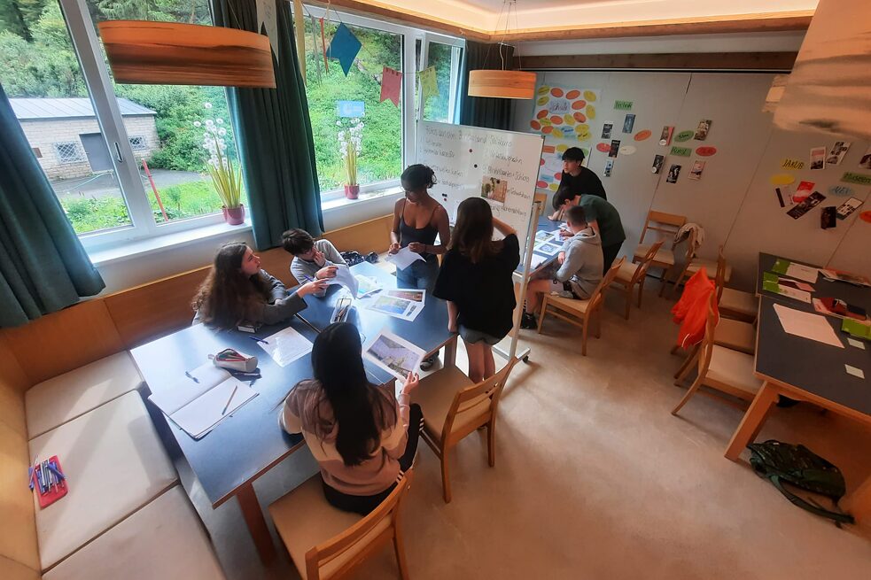 Jugendliche in einem Klassenraum sitzen an Tischen von verschiedenen Unterlagen.
