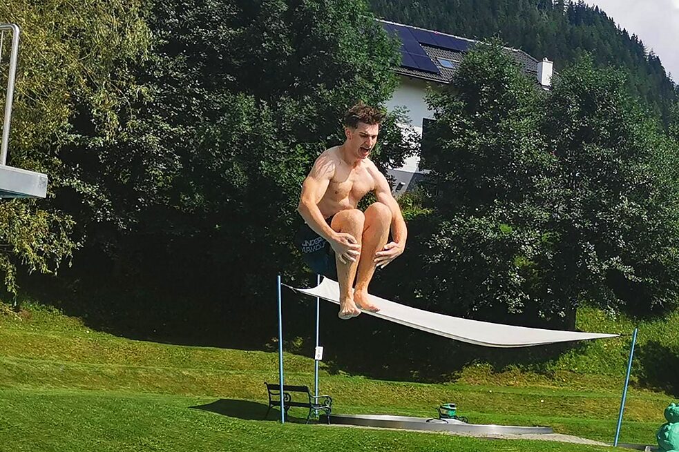 Ein junger Erwachsener spring von einem Turm in einen Pool.