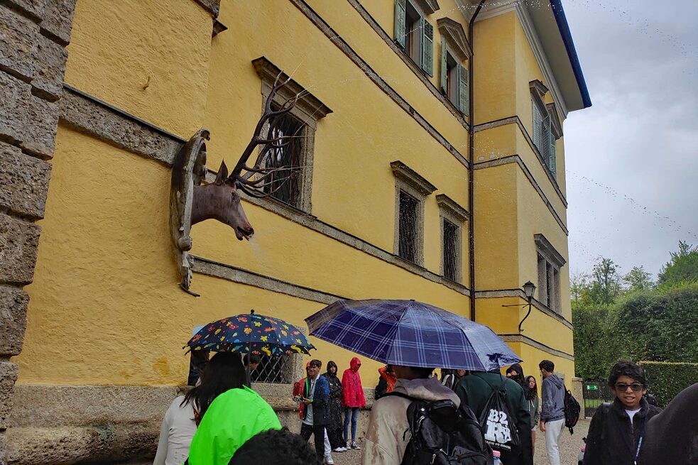 Jugendliche stehen unter Regenschirmen am Schloss Hellbrunn.