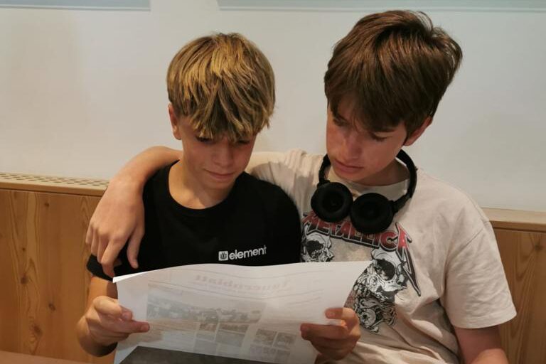 Jugendliche in einer Mensa halten einen großen Bogen Papier in der Hand und lesen.