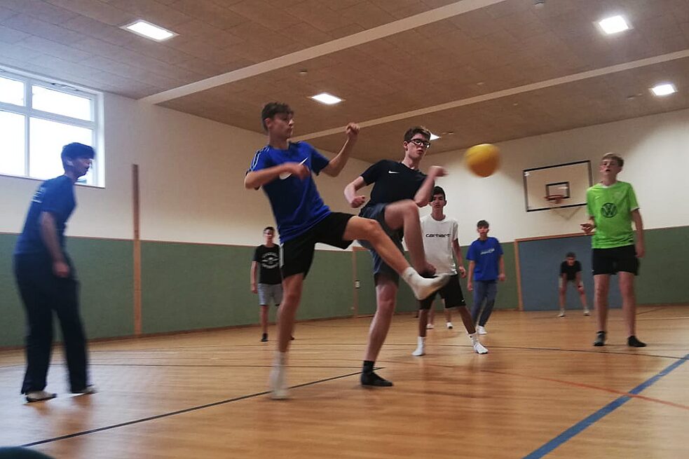 Jugendliche spielen Fußball in einer Halle.