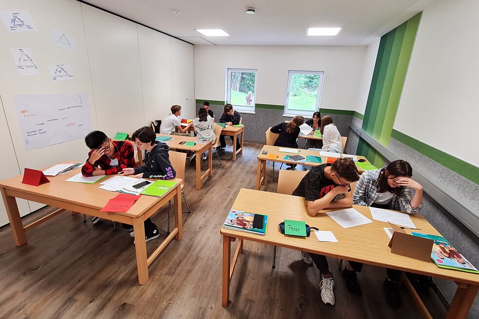 Jugendliche in einem Klassenraum sitzen an Tischen und arbeiten konzentriert.