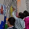 Drei Kinder malen auf einer großen Leinwand, auf der das Streetart-Werk des Kunstkollektivs ArtLords entsteht © © Goethe-Institut im Exil  Partizipatives Mural des Kunstkollektivs ArtLords