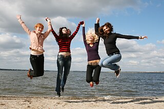 Eine Gruppe Mädchen springt in die Luft. Im Hintergrund das Meer.