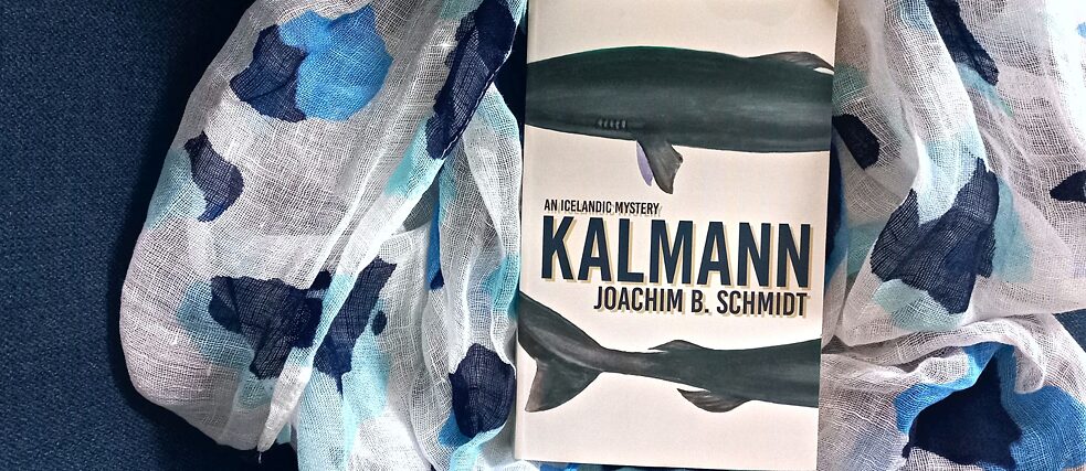 The book 'Kalmann', depicts sharks and is lying on a blue & white scarf