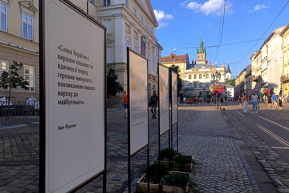 Lwiw, Juli 2023: Auf dem Marktplatz stehen stets aktuelle Gedenktafeln für gefallene Soldat*innen. Dem vorangestellt ist ein Zitat von Iwan Franko (1856-1916): „‚Ruhm der Ukraine‘ ist ein Ausdruck von Wertschätzung und Dankbarkeit gegenüber den Helden der Vergangenheit sowie eine Aufforderung unseres Volkes für die Zukunft.“