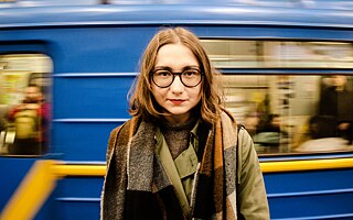 Mladá žena stojí pred žlto-modrým vagónom vlaku
