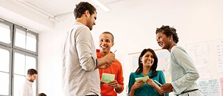 Four participants laugh as they stand in a circle and play an ice-breaker game.
